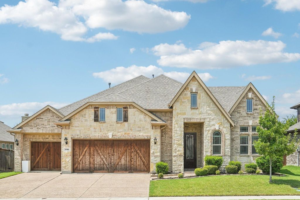 View of front of house featuring a shingled roof, concrete driveway, stone siding, a front lawn, and a garage