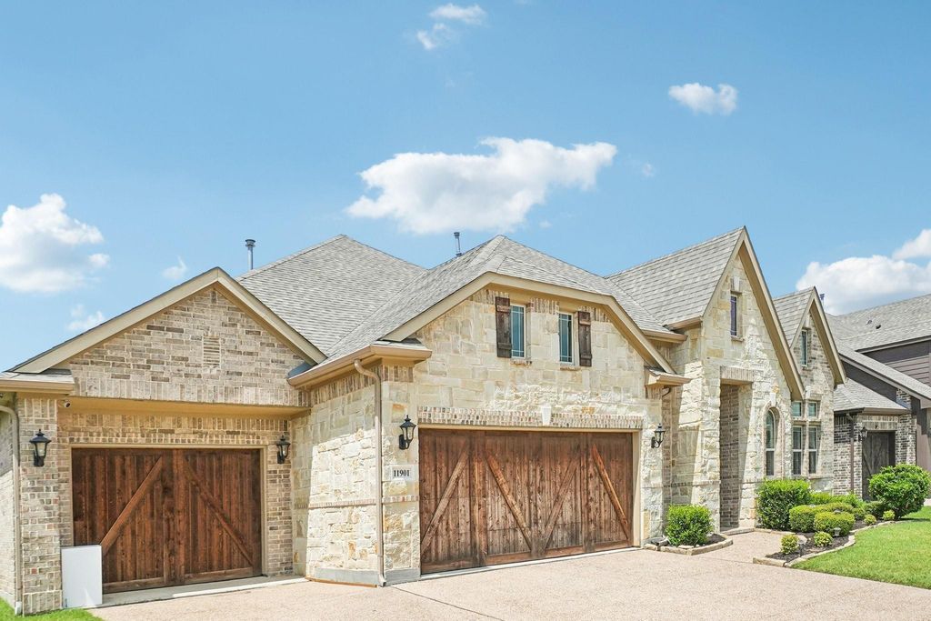 French country style house featuring stone siding, a shingled roof, driveway, an attached garage, and brick siding