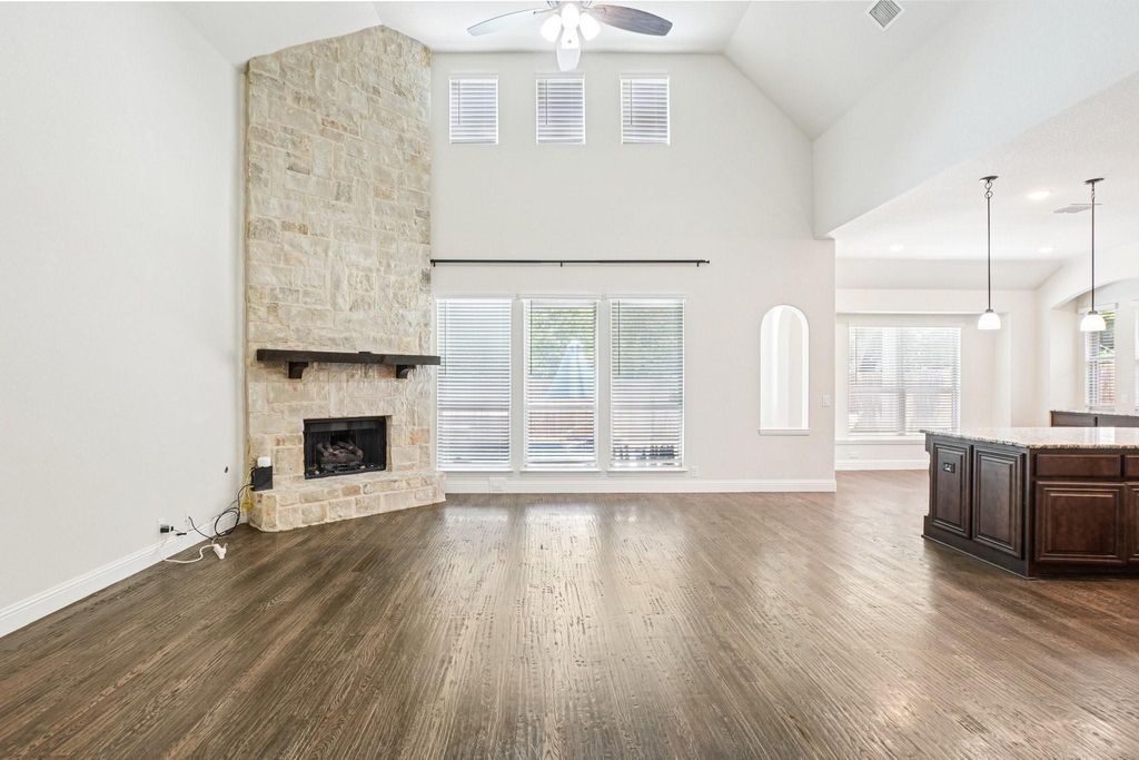 Unfurnished living room featuring healthy amount of natural light, dark wood-style floors, a stone fireplace, and high vaulted ceiling