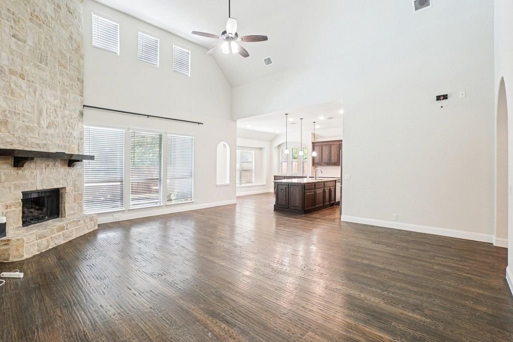 Unfurnished living room featuring healthy amount of natural light, high vaulted ceiling, dark wood-type flooring, arched walkways, and a fireplace