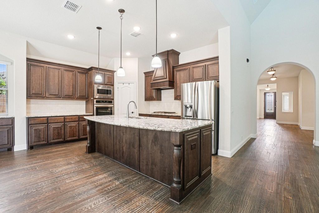 Kitchen featuring arched walkways, tasteful backsplash, light stone countertops, pendant lighting, and recessed lighting