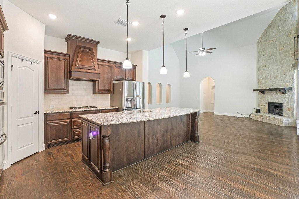 Kitchen featuring backsplash, decorative light fixtures, an island with sink, light stone countertops, and open floor plan