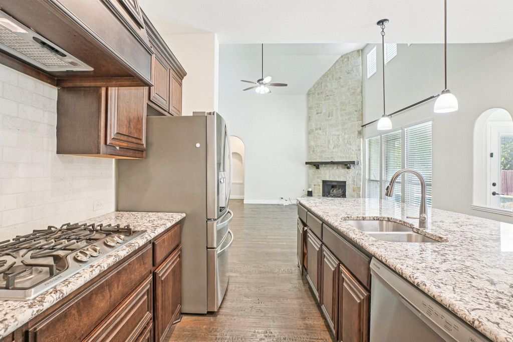 Kitchen featuring dark wood-style flooring, light stone counters, backsplash, stainless steel appliances, and arched walkways