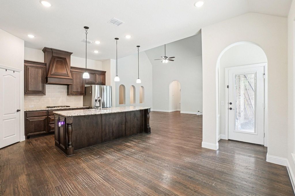 Kitchen with lofted ceiling, dark brown cabinets, backsplash, pendant lighting, and a kitchen island with sink
