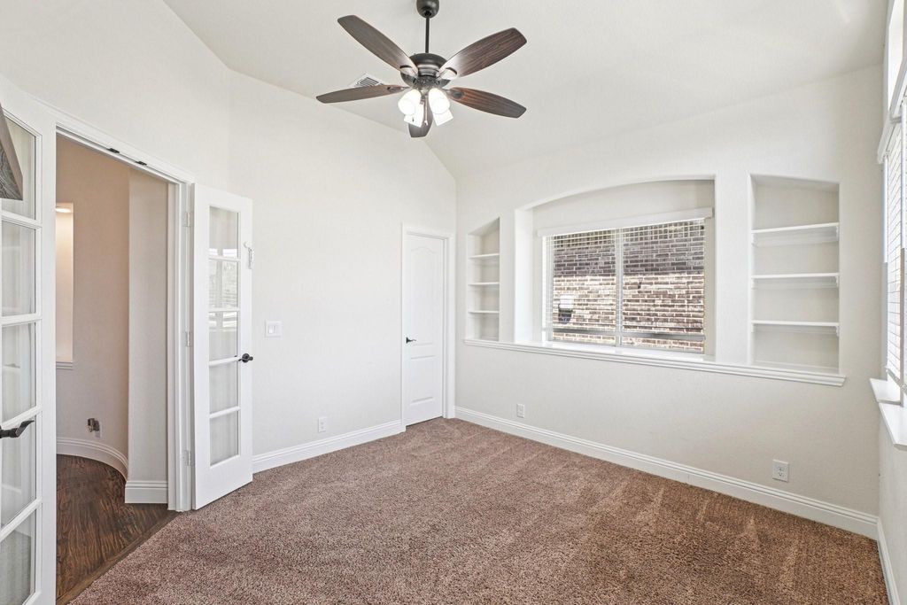 Spare room with built in shelves, dark colored carpet, a ceiling fan, and lofted ceiling