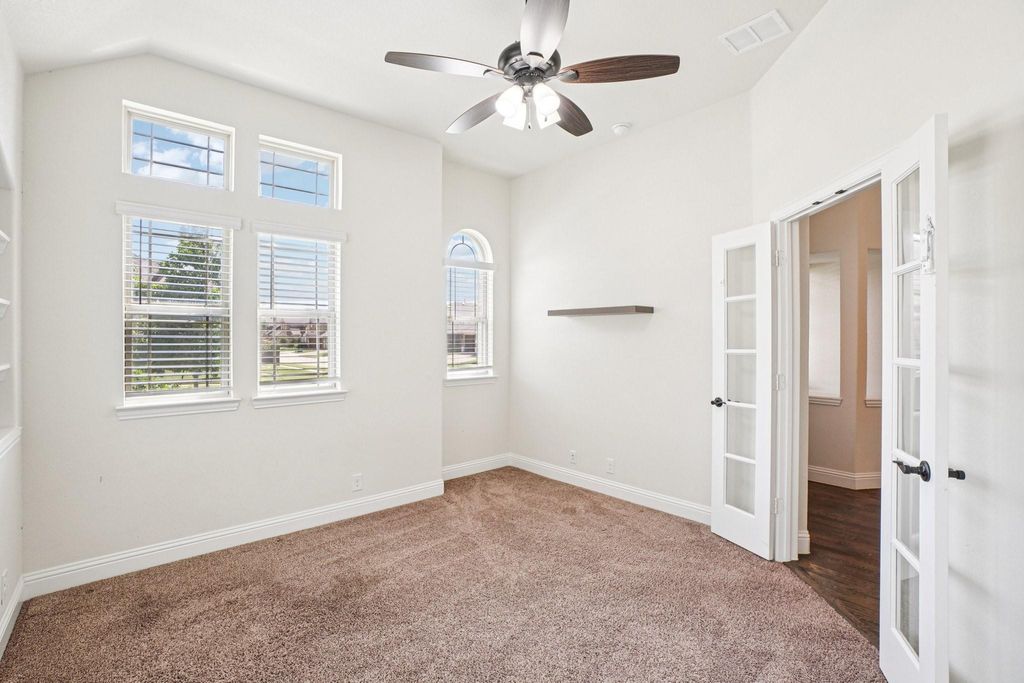 Carpeted spare room featuring a ceiling fan, french doors, and lofted ceiling