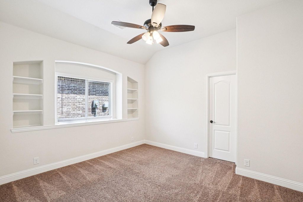 Spare room featuring built in shelves, carpet floors, lofted ceiling, and ceiling fan