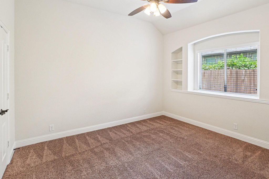Spare room featuring built in shelves, dark carpet, a ceiling fan, and lofted ceiling