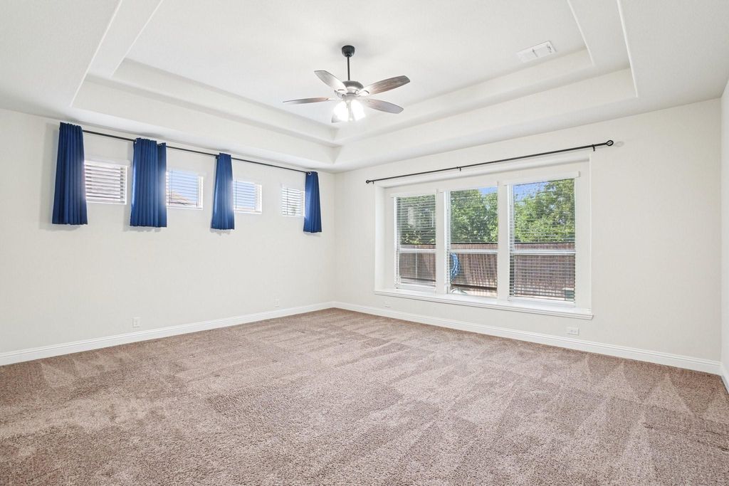 Empty room featuring a tray ceiling, light colored carpet, and ceiling fan