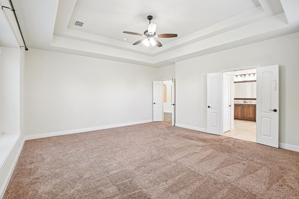 Unfurnished bedroom featuring light colored carpet, a raised ceiling, ceiling fan, and ensuite bath
