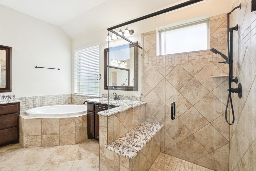 Bathroom featuring healthy amount of natural light, two vanities, a stall shower, and vaulted ceiling
