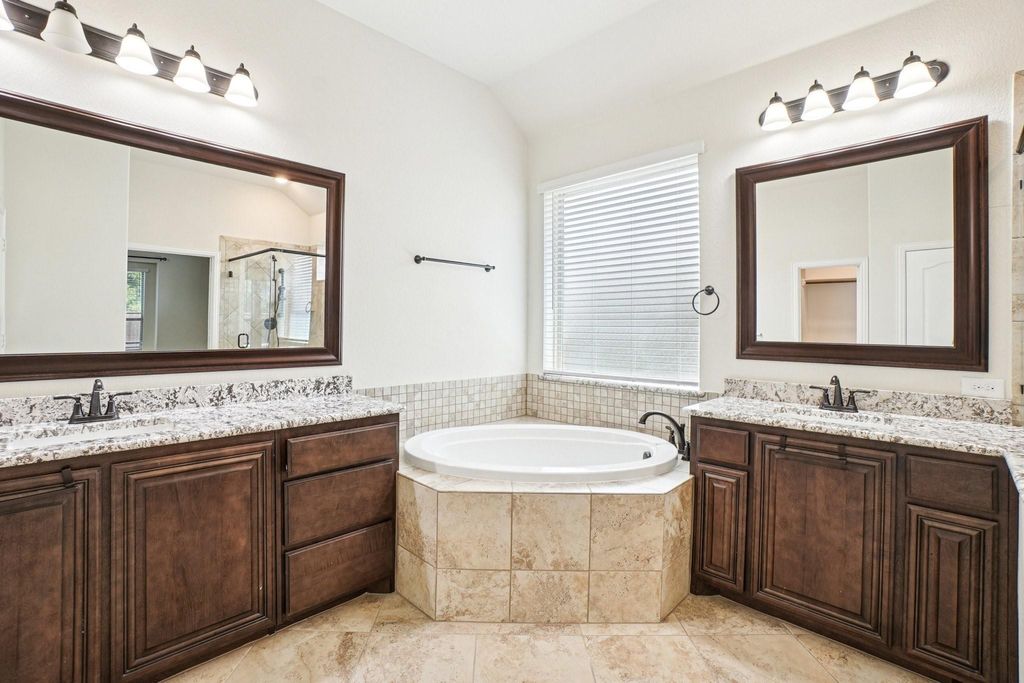 Bathroom featuring a shower stall, two vanities, a bath, vaulted ceiling, and light tile patterned floors