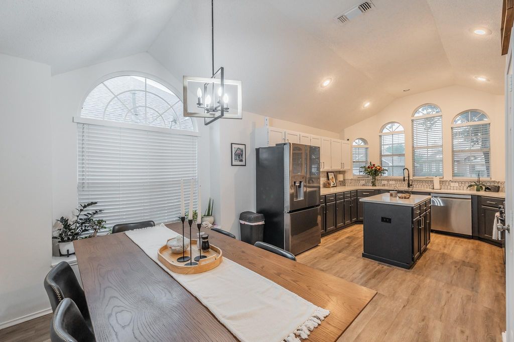 Kitchen featuring vaulted ceiling, light wood-type flooring, appliances with stainless steel finishes, a center island, and decorative light fixtures