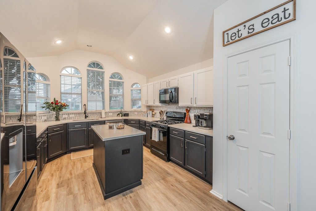 Kitchen with dark cabinets, black appliances, lofted ceiling, a kitchen island, and light wood-style floors
