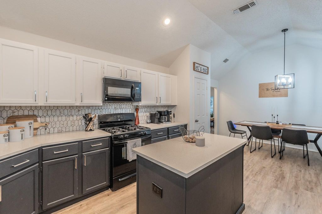 Kitchen featuring black appliances, decorative backsplash, white cabinetry, a center island, and vaulted ceiling