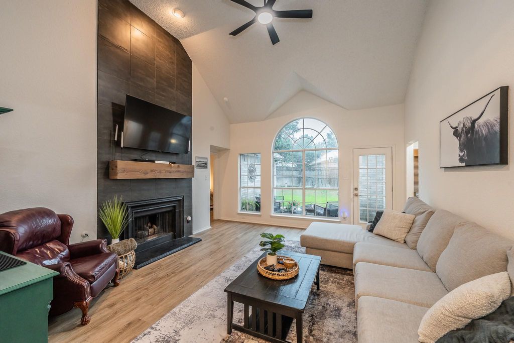 Living area featuring high vaulted ceiling, wood finished floors, a tile fireplace, and ceiling fan