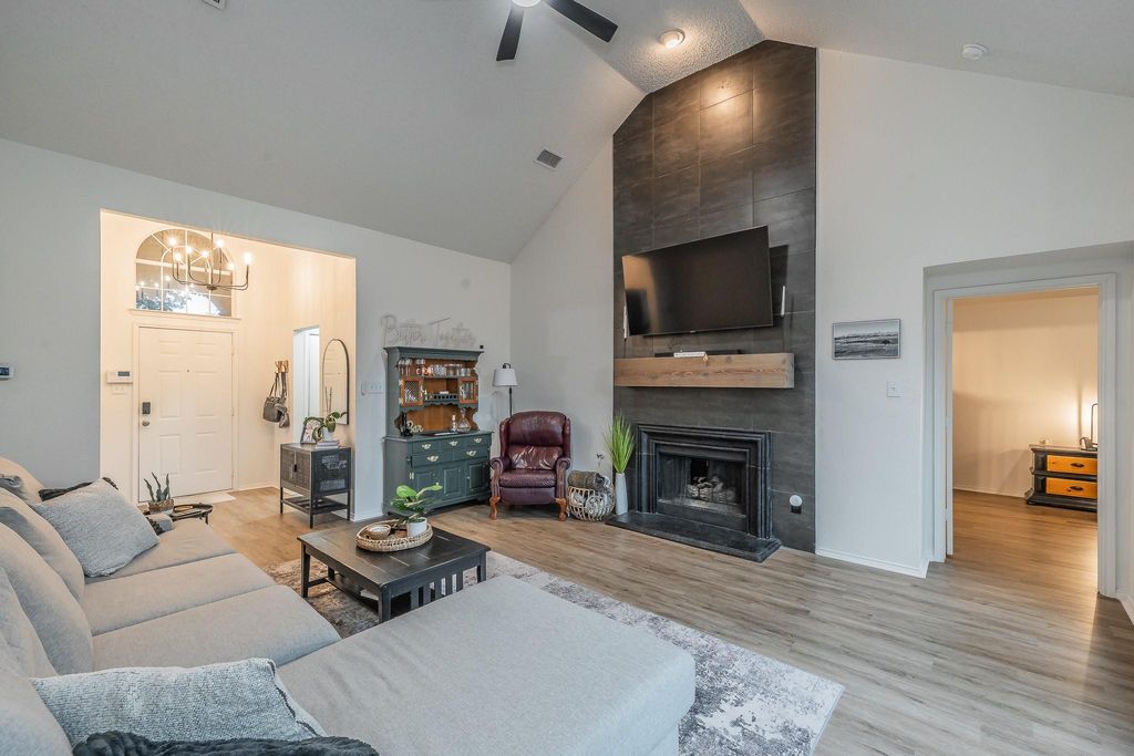 Living room featuring high vaulted ceiling, light wood-type flooring, a fireplace, a chandelier, and a ceiling fan