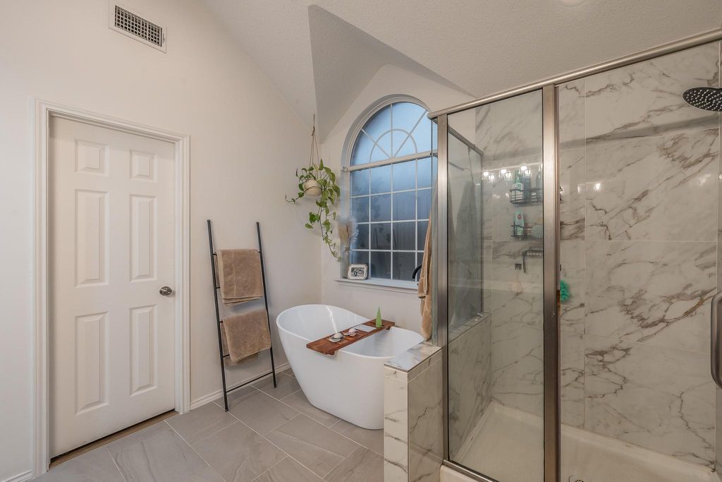 Full bath featuring a marble finish shower, a freestanding bath, and lofted ceiling
