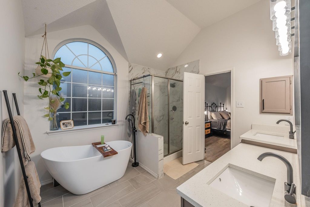 Ensuite bathroom featuring a freestanding tub, double vanity, lofted ceiling, a marble finish shower, and light tile patterned floors
