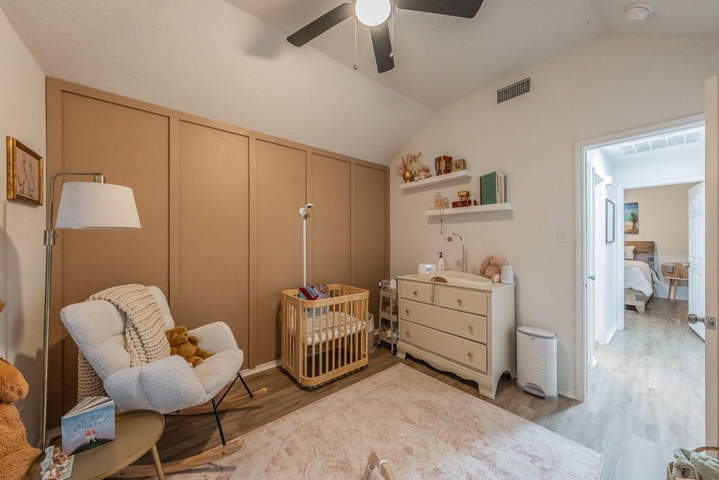Bedroom featuring lofted ceiling, light wood finished floors, a crib, and a ceiling fan