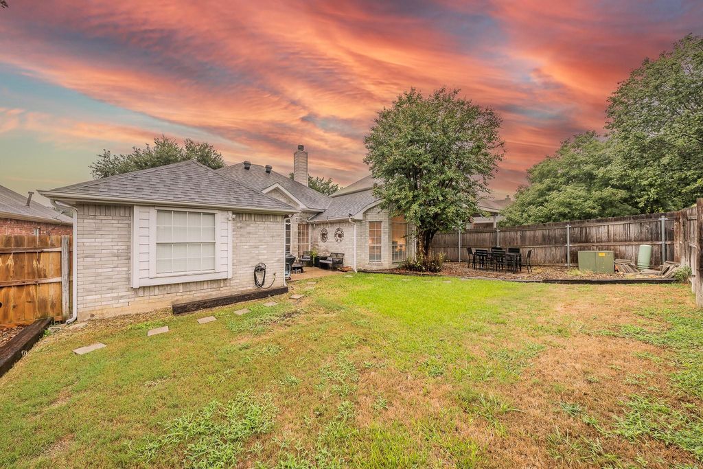 Back of property at dusk featuring a fenced backyard, brick siding, a chimney, and roof with shingles