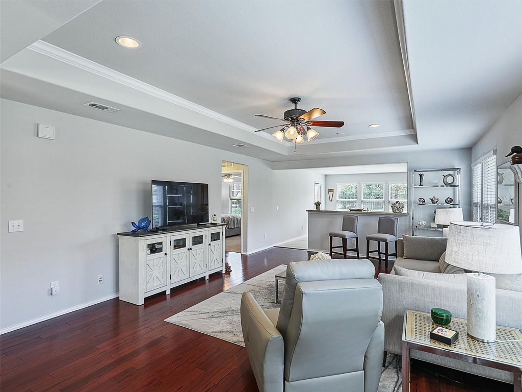 Living room featuring a tray ceiling, dark wood-style floors, plenty of natural light, a ceiling fan, and ornamental molding