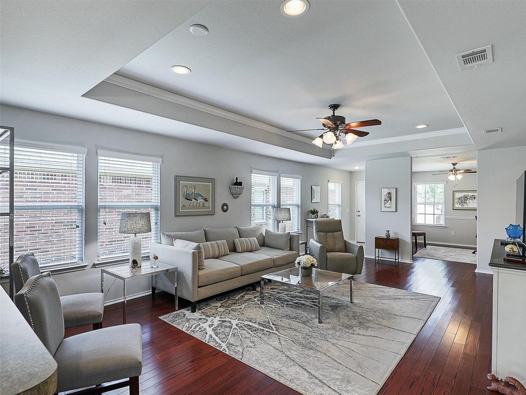 Living area with a raised ceiling, dark wood-type flooring, recessed lighting, ceiling fan, and ornamental molding