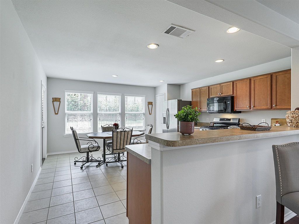 Kitchen featuring brown cabinets, a peninsula, light tile patterned floors, appliances with stainless steel finishes, and recessed lighting