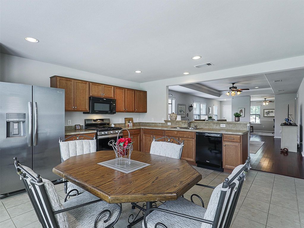Kitchen featuring light tile patterned flooring, black appliances, a tray ceiling, brown cabinets, and a peninsula