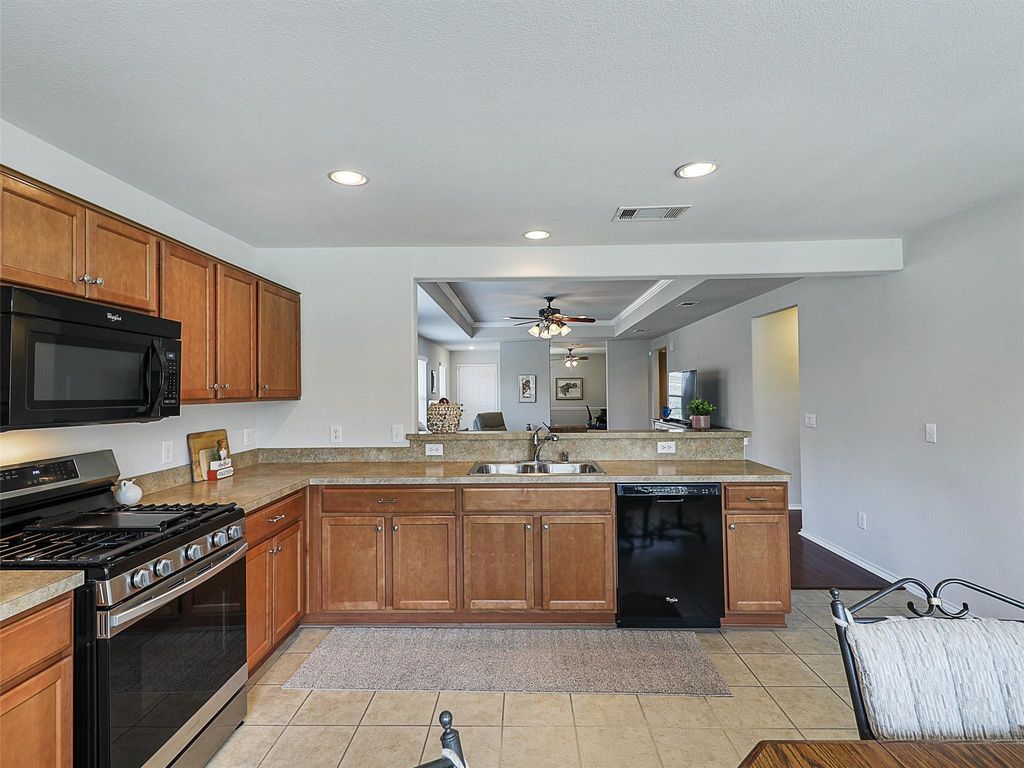 Kitchen featuring black appliances, a peninsula, brown cabinets, a tray ceiling, and light tile patterned floors