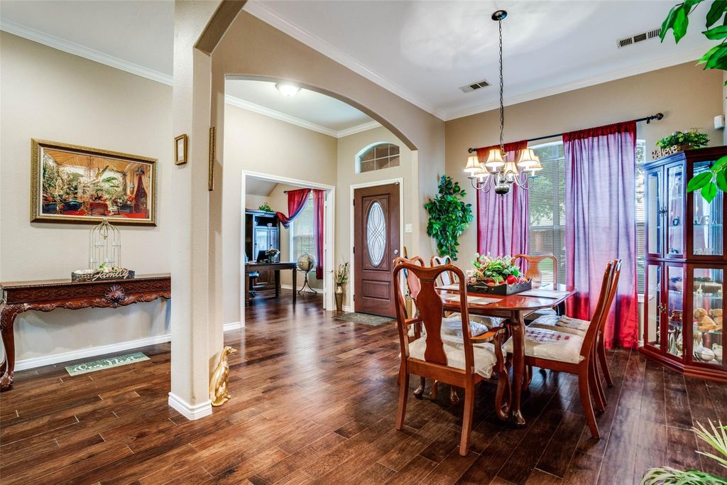 Dining space with arched walkways, dark wood-type flooring, ornamental molding, and a chandelier