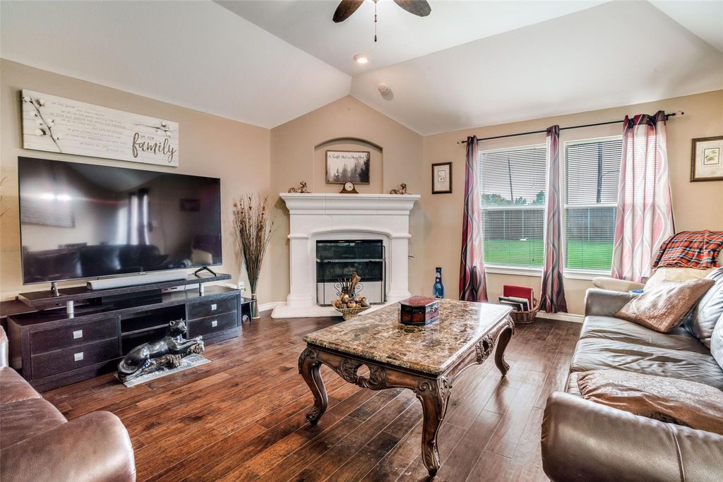 Living room featuring lofted ceiling, hardwood / wood-style floors, a ceiling fan, and a glass covered fireplace