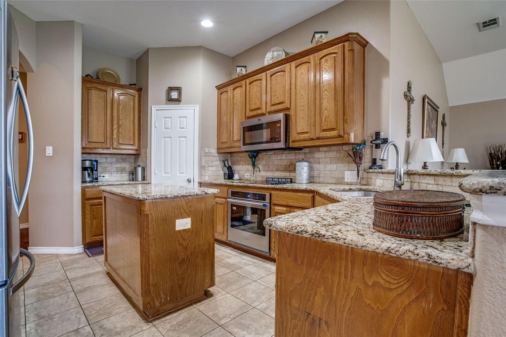 Kitchen with brown cabinetry, light stone counters, decorative backsplash, and a kitchen island