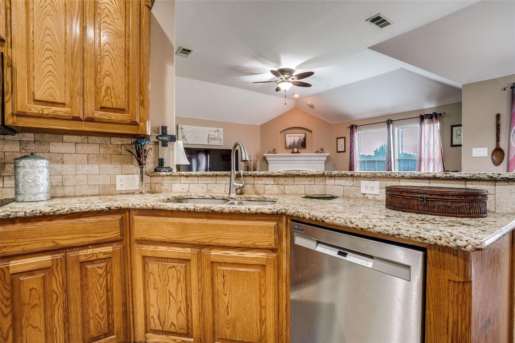 Kitchen featuring brown cabinetry, stainless steel dishwasher, light stone counters, decorative backsplash, and lofted ceiling