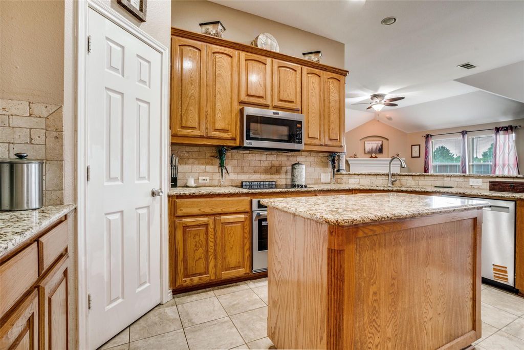 Kitchen with light stone countertops, vaulted ceiling, light tile patterned floors, a center island, and backsplash