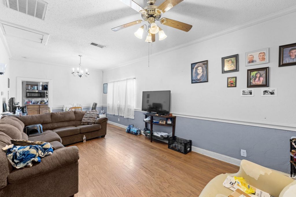 Living area featuring a textured ceiling, wood finished floors, ceiling fan, ornamental molding, and a chandelier