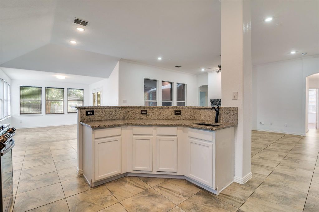 Kitchen featuring arched walkways, white cabinetry, open floor plan, dark stone counters, and stainless steel gas range oven