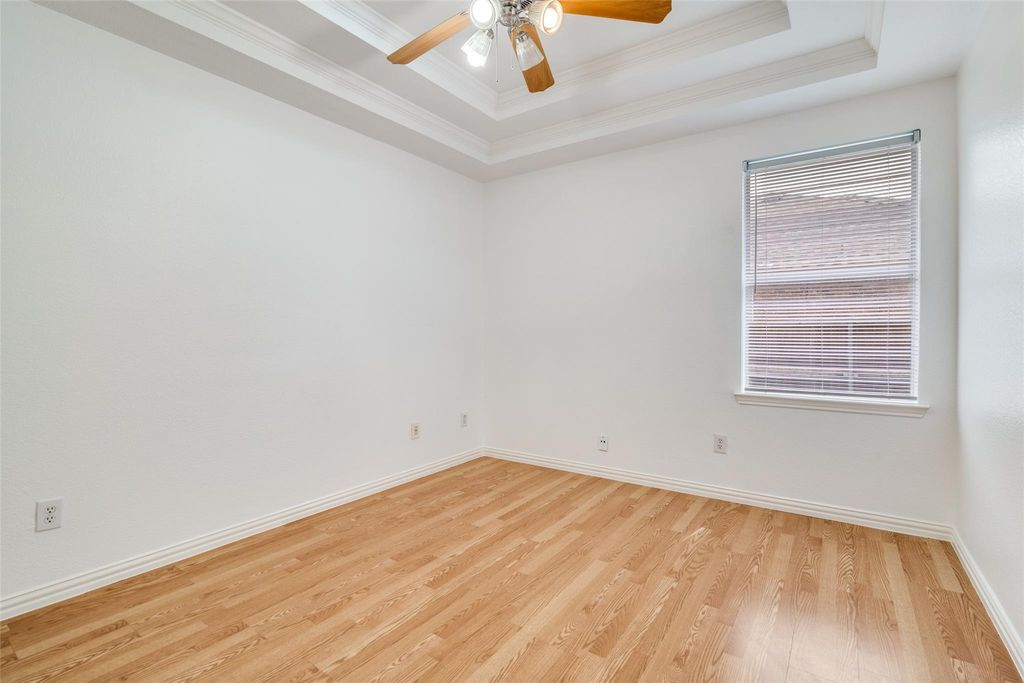Bedroom featuring a tray ceiling, light wood-type flooring, crown molding, and a ceiling fan