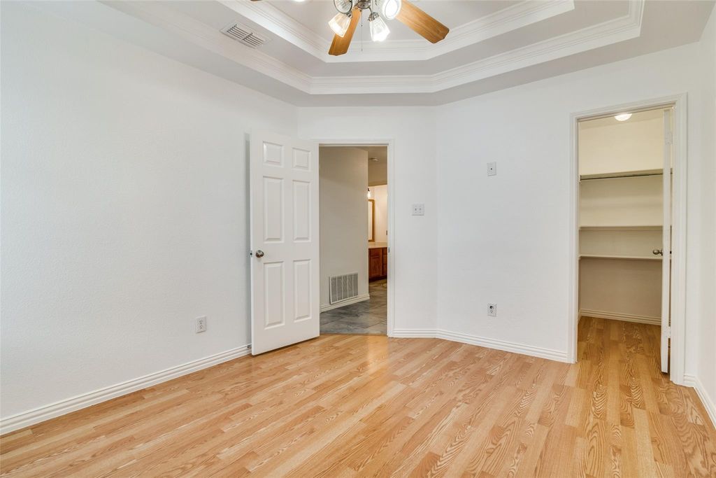 Bedroom with a tray ceiling, ornamental molding, light wood finished floors, a walk in closet, and a ceiling fan