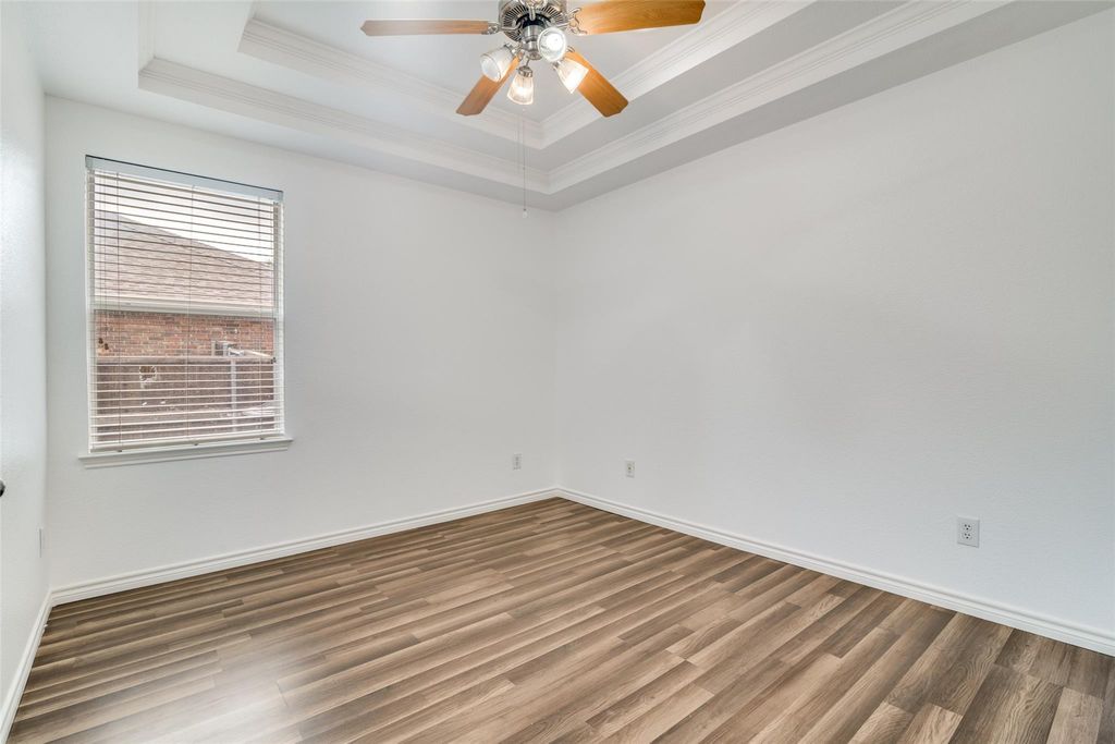 Bedroom with a raised ceiling, wood finished floors, ornamental molding, and ceiling fan