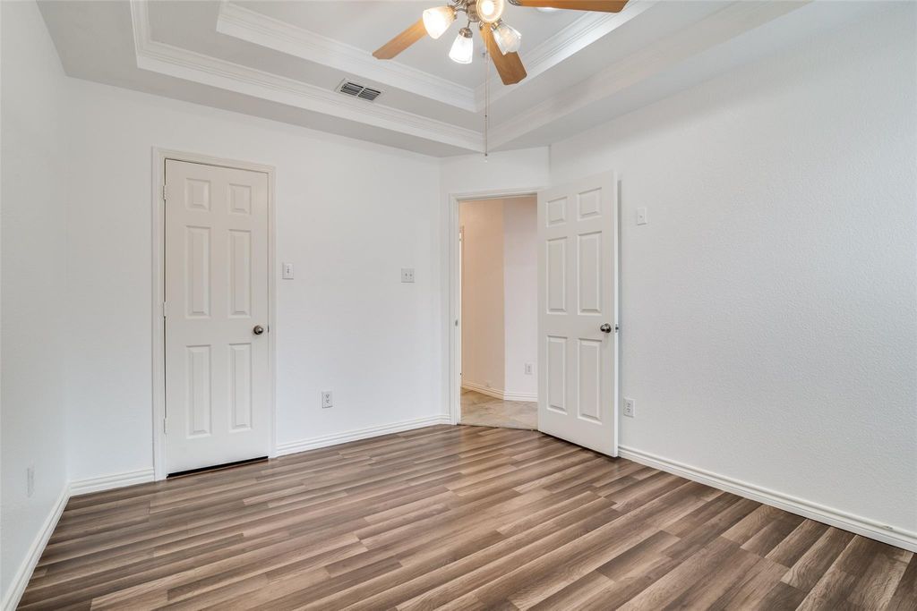 Bedroom with a raised ceiling, wood finished floors, ornamental molding, and ceiling fan