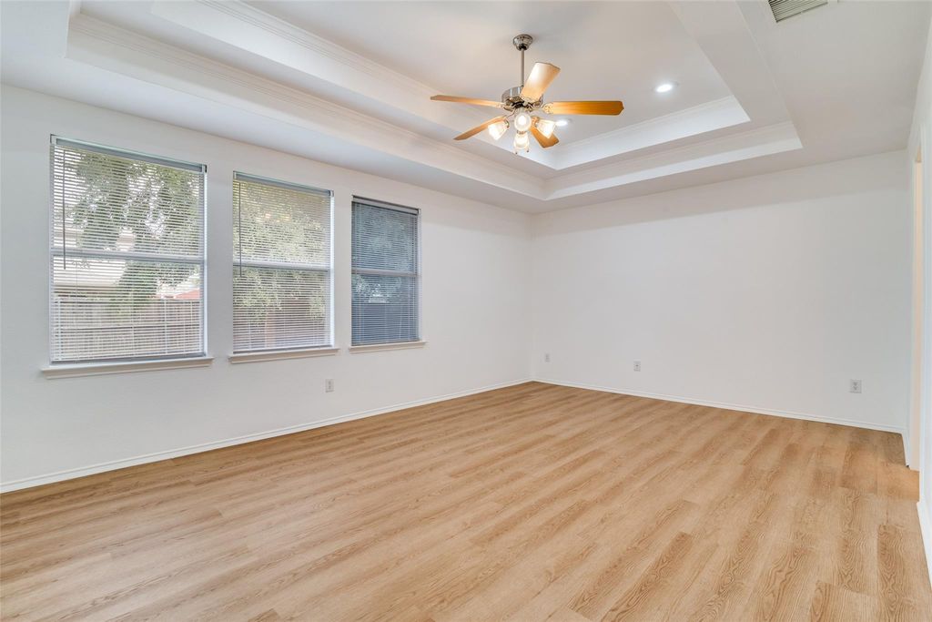 Bedroom featuring a raised ceiling, crown molding, light wood-style flooring, and ceiling fan