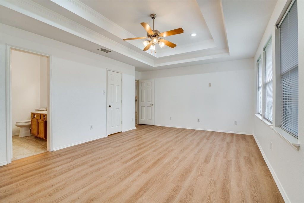 Bedroom with a raised ceiling, light wood-type flooring, ceiling fan, connected bathroom, and crown molding