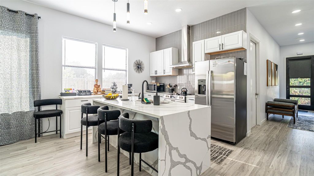 Kitchen featuring stainless steel appliances, a breakfast bar area, a kitchen island with sink, light stone counters, and light wood finished floors