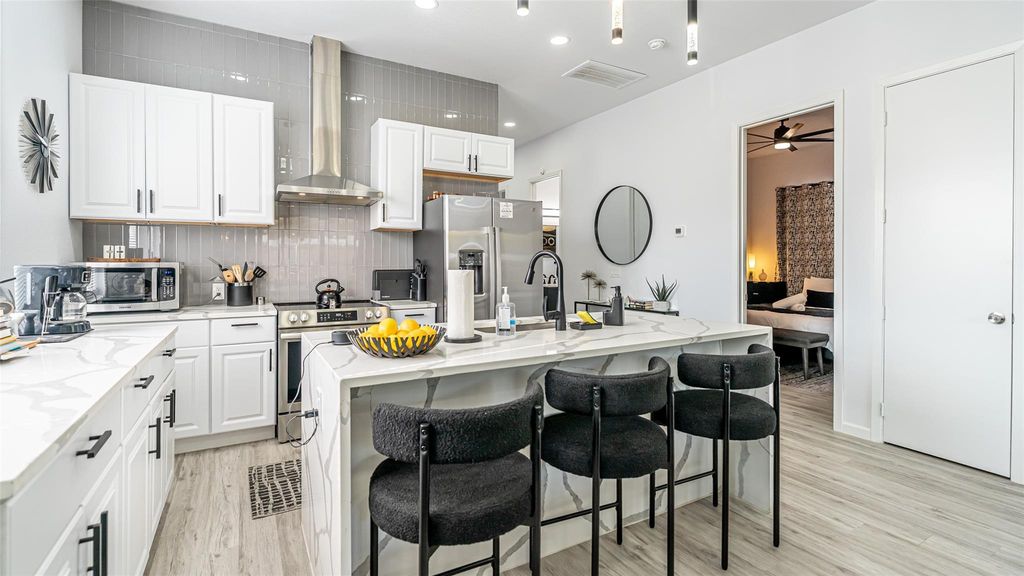 Kitchen featuring tasteful backsplash, wall chimney exhaust hood, an island with sink, light stone countertops, and recessed lighting