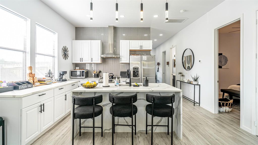 Kitchen with tasteful backsplash, light stone countertops, wall chimney exhaust hood, white cabinets, and light wood finished floors