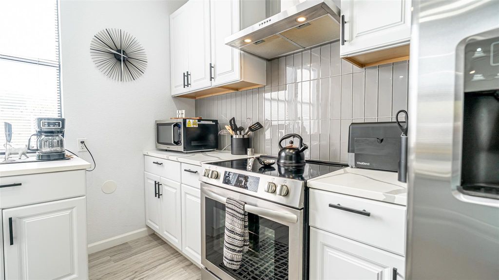 Kitchen with stainless steel appliances, under cabinet range hood, white cabinetry, light countertops, and tasteful backsplash