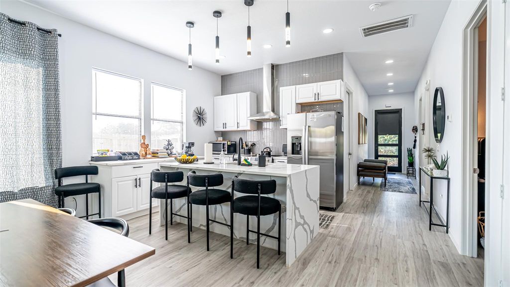 Kitchen featuring a breakfast bar, an island with sink, stainless steel refrigerator with ice dispenser, decorative backsplash, and wall chimney exhaust hood