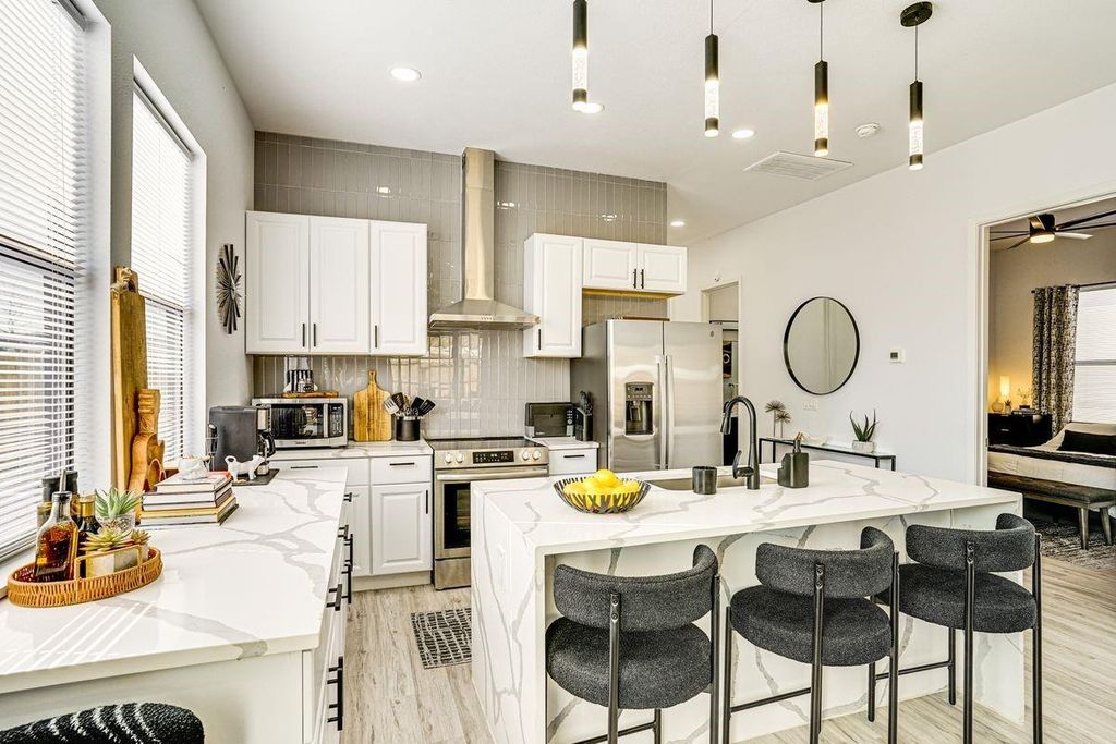 Kitchen featuring backsplash, a breakfast bar, appliances with stainless steel finishes, wall chimney range hood, and light stone countertops