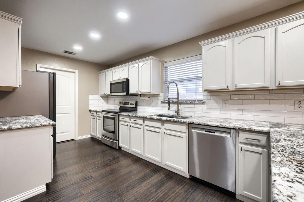 Kitchen with stainless steel appliances, decorative backsplash, light stone counters, dark wood finished floors, and white cabinetry